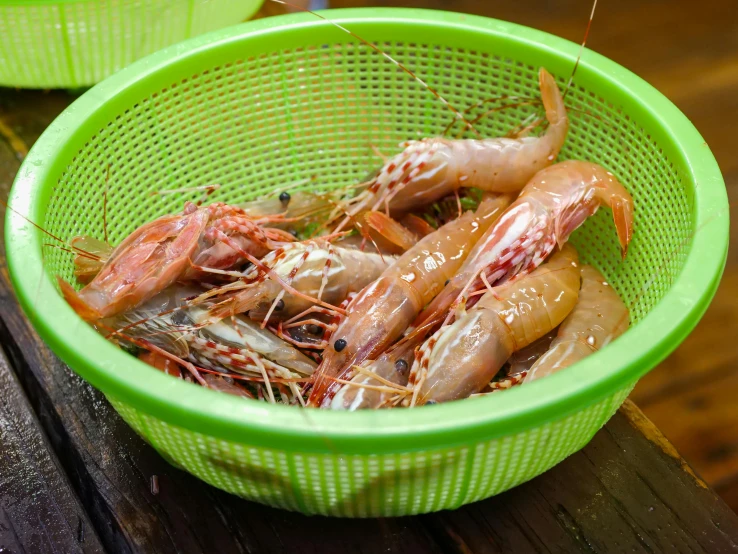 a green bowl filled with shrimp sitting on top of a wooden table, wet market street, pink axolotl in a bucket, thumbnail, mediterranean