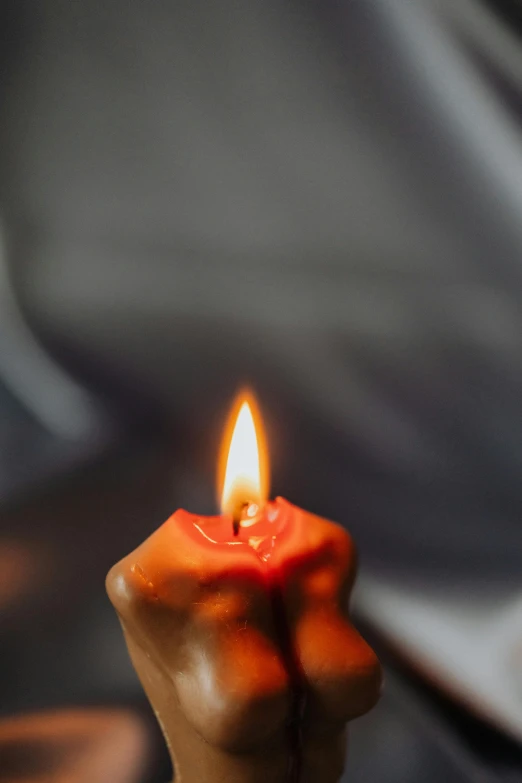 a hand holding a lit candle on a table, bright red, medium head to shoulder shot, on a gray background, doing a prayer