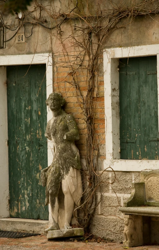 a stone statue sitting next to a green door, inspired by Marià Fortuny, dilapidated houses, venice, dried vines, 1800