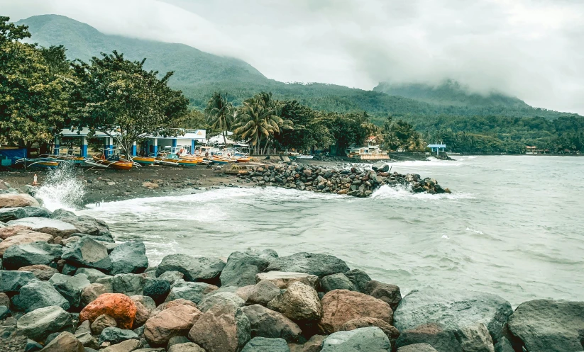 a rocky beach next to a body of water, by Andrée Ruellan, pexels contest winner, mountainous jungle setting, small port village, black sand, background image