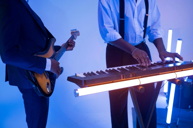 a couple of men standing next to each other in front of a keyboard, an album cover, unsplash, bright glowing instruments, dramatic white and blue lighting, musicians playing instruments, wedding