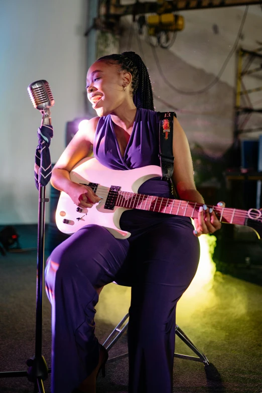 a woman sitting on a chair playing a guitar, by Ella Guru, happening, lit up, slightly smiling, african sybil, performance