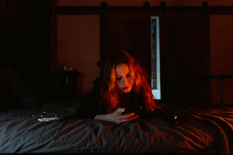 a woman laying on a bed using a cell phone, a portrait, inspired by Nan Goldin, pexels, digital art, red glowing hair, gaming, emerging from her lamp, spooky photo