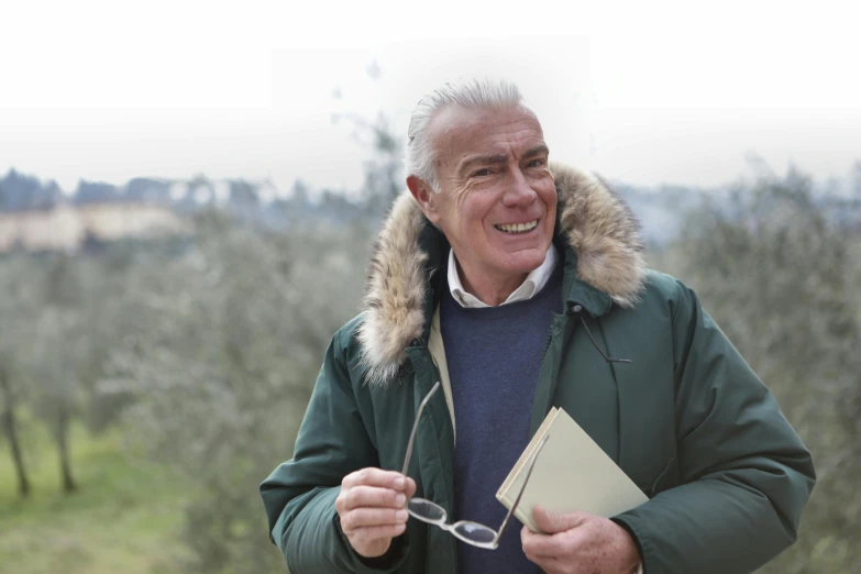 a man in a parka holding a book and a pair of scissors, inspired by Vito D'Ancona, pexels contest winner, delightful surroundings, older male, italian looking emma, giorgetto giugiaro