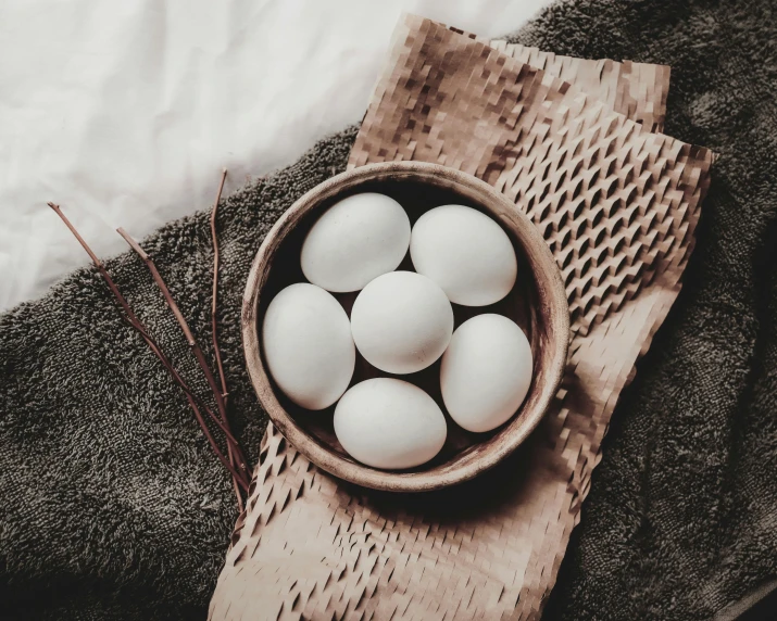 a wooden bowl filled with eggs on top of a towel, by Emma Andijewska, trending on pexels, renaissance, hair, dragon eggs, white, instagram picture