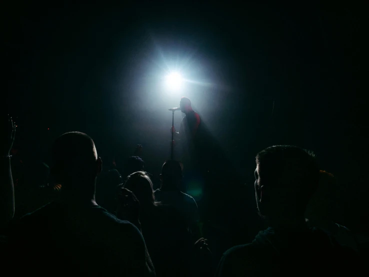 a group of people standing in front of a light, happening, spotlight on the singer, out in the dark, instagram post, back light contrast