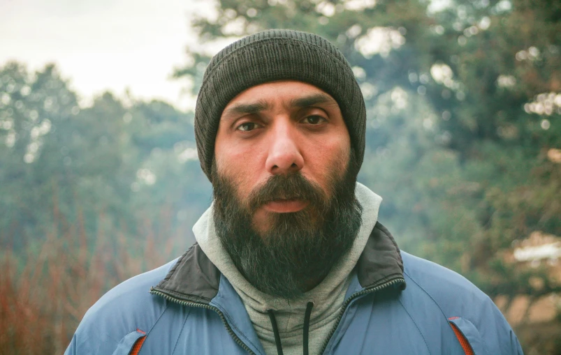 a man with a beard wearing a blue jacket, by Muggur, pexels contest winner, hyperrealism, still from a terence malik film, he also wears a grey beanie, (fire), wideangle portrait