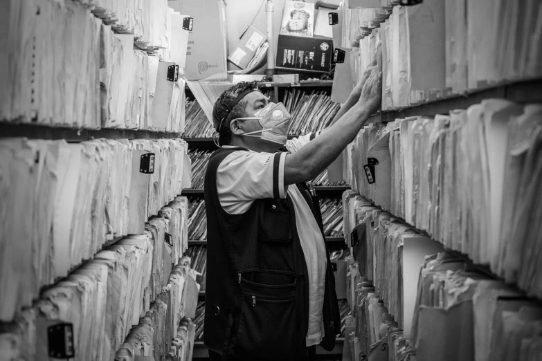 a black and white photo of a man in a library, an album cover, pexels, process art, healthcare worker, inspect in inventory image, rack, masked person in corner