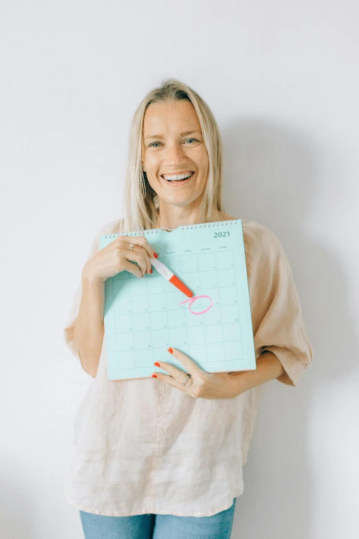 a woman holding a piece of paper with writing on it, female calendar, penned in cyan ink, looking happy, holding pencil