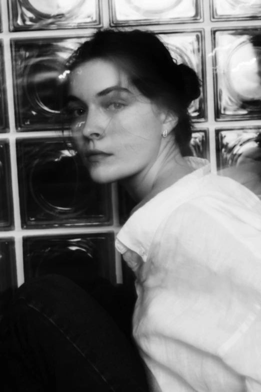 a black and white photo of a woman in front of a glass block wall, inspired by Emma Andijewska, tumblr, brooke shields, zoomed in, ansel ], she is wearing a hat