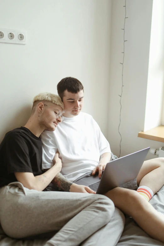 two men sitting on a bed looking at a laptop, by Carey Morris, pexels, renaissance, non binary model, holding each other, very pale, sitting on the couch