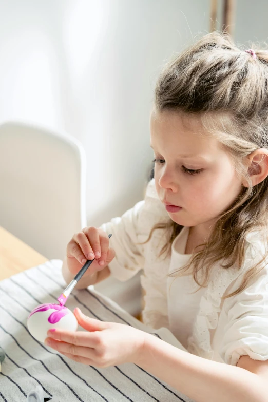 a little girl that is sitting at a table, an airbrush painting, pexels contest winner, an egg, holding a paintbrush, crisp smooth clean lines, topknot