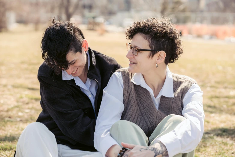 a couple of people sitting on top of a grass covered field, an album cover, by Ellen Gallagher, pexels, lesbians, orthodox, springtime, androgyny