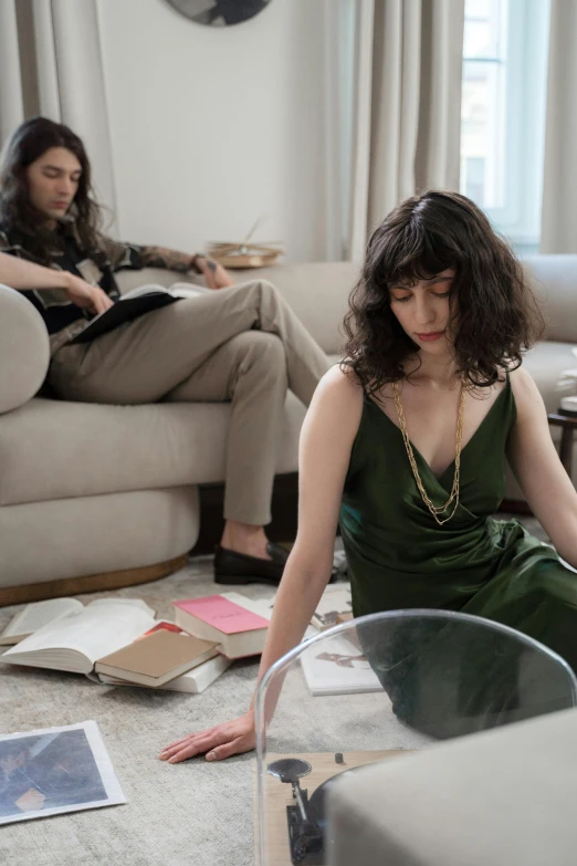 a woman in a green dress sitting on the floor, an album cover, inspired by Nan Goldin, trending on pexels, an elegant couple, reading for a party, finn wolfhard, dwell