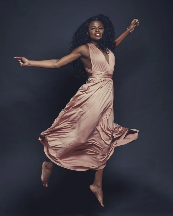 a woman in a pink dress jumping in the air, an album cover, by Arabella Rankin, unsplash, happening, with brown skin, wearing an evening gown, confident pose, model posing