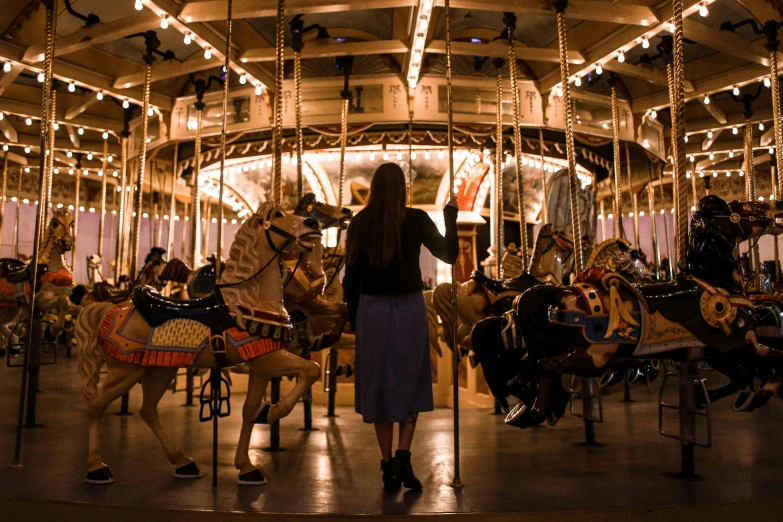 a woman is standing in front of a carousel, pexels contest winner, rex orange county, under a spotlight, 🦩🪐🐞👩🏻🦳, san francisco