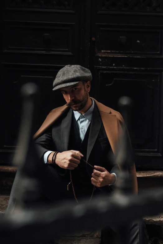a man sitting on the steps of a building looking at his cell phone, a portrait, inspired by Max Magnus Norman, pexels contest winner, costumes from peaky blinders, hand holding cap brim, thumbnail, coat pleats