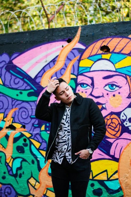 a man standing in front of a colorful wall, inspired by Robbie Trevino, trending on pexels, graffiti, asian male, pete davidson, vivid)