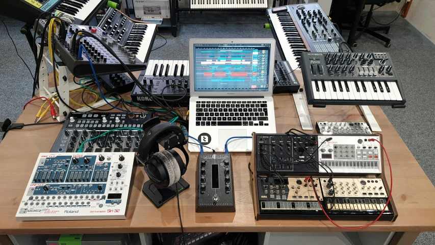 a laptop computer sitting on top of a wooden table, an album cover, by Joe Bowler, unsplash, computer art, piles of modular synth cables, devices and instruments, in his basement studio, taken on iphone 14 pro