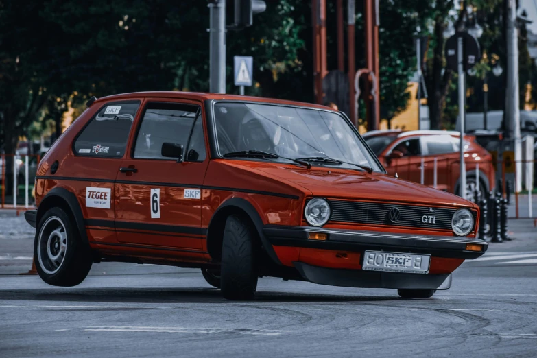 a red car driving down a city street, a photo, by Adam Marczyński, pexels contest winner, hyperrealism, orange racing stripes, square, rally car, slavic style