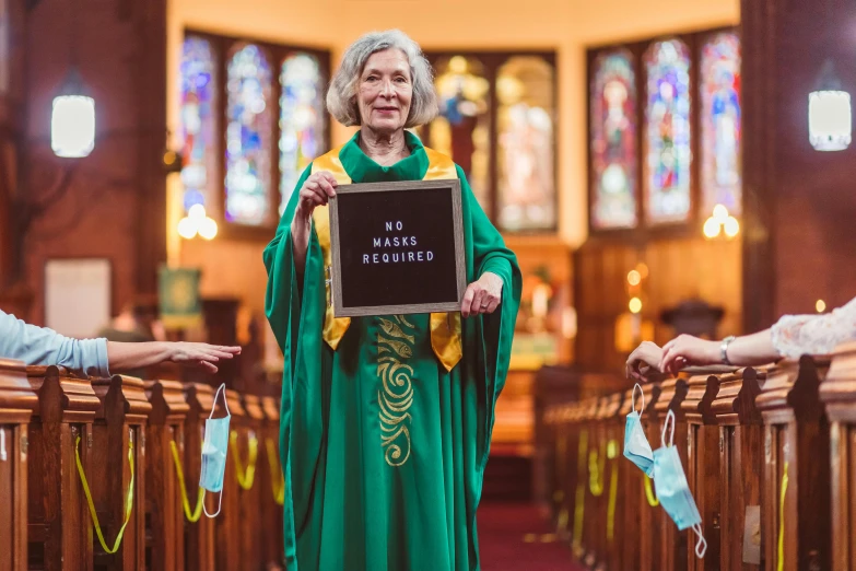 a woman standing in a church holding a sign, green robes, photograph taken in 2 0 2 0, james webb, 7 0 years old