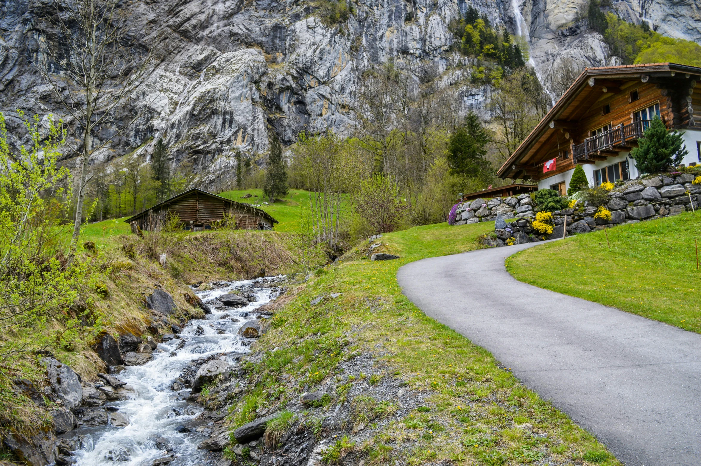 a small stream running through a lush green hillside, by Franz Hegi, pexels contest winner, wooden houses, lauterbrunnen valley, paved roads, avatar image