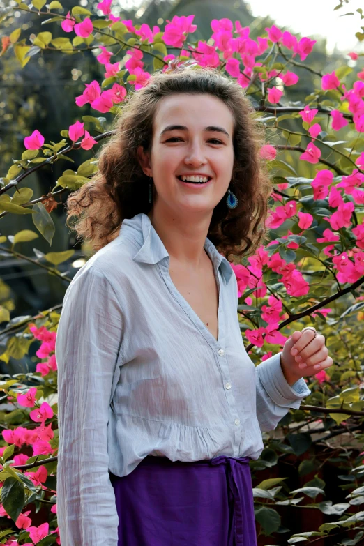 a woman standing in front of a bush of flowers, wearing a light shirt, portrait sophie mudd, bougainvillea, student