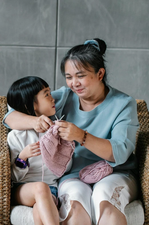 a woman sitting on top of a chair next to a little girl, inspired by Ruth Jên, pexels contest winner, crochet, asian, cardigan, thumbnail