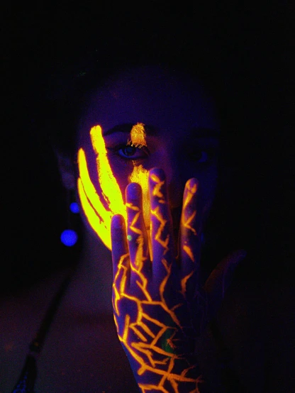 a woman holding her hand up to her face in the dark, a picture, inspired by Elsa Bleda, pexels, holography, day - glow facepaint, yellow skin, neon hand sports bracelet, intricate illuminated lines