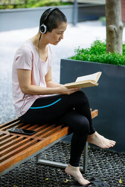 a woman sitting on a bench reading a book, happening, wearing modern headphone, no ears, australian, vietnamese woman