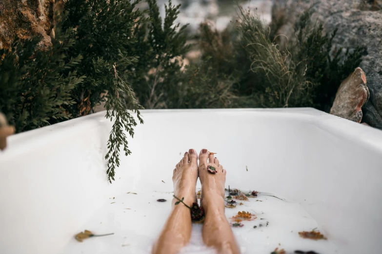 a person laying in a bathtub with their feet in the water, a photo, by Julia Pishtar, trending on pexels, botanicals, glamping, manuka, with soft bushes