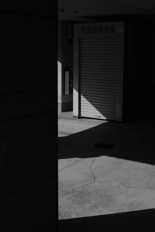 a black and white photo of an open garage door, inspired by Arnold Newman, unsplash, postminimalism, in the streets of tokyo, volumetric shadows, in a square, dark aesthetic