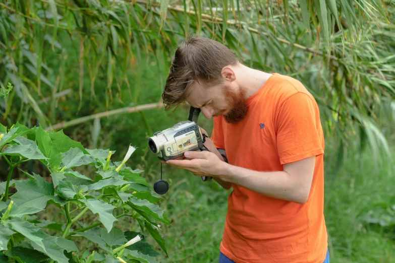 a man that is standing in the grass with a camera, next to a plant, permaculture, avatar image