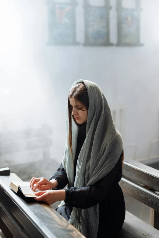 a woman sitting in a church reading a book, inspired by Modest Urgell, black scarf, gray, 2019 trending photo, handsome girl