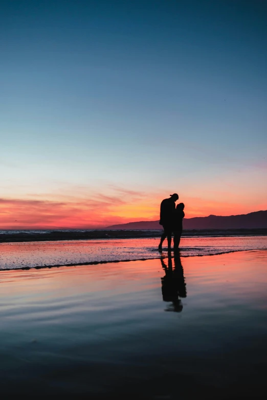 a couple standing on the beach at sunset, by Lee Loughridge, unsplash contest winner, reflection, phot, profile pic