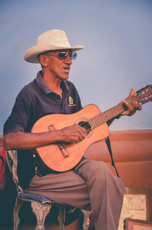 a man sitting on a chair playing a guitar, an album cover, inspired by Albert Namatjira, pexels contest winner, happening, wearing a travel hat, an oldman, colombian, profile pic