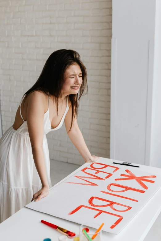 a woman standing in front of a table with a sign on it, pexels contest winner, seducing expression, young asian woman, white box, designer product