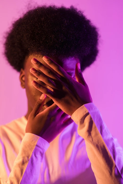 a woman covering her face with her hands, inspired by Carrie Mae Weems, trending on pexels, afrofuturism, pink violet light, black man with afro hair, androgynous person, concert photo