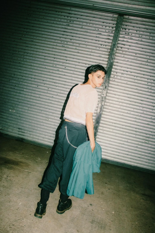 a man standing in front of a garage door, an album cover, inspired by Elsa Bleda, unsplash, renaissance, attractive girl tomboy, baggy pants, nishihara isao, non binary model