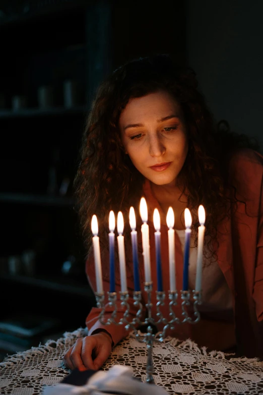 a woman blowing out candles on a menorah, digital still, comforting, movie photo, holiday season