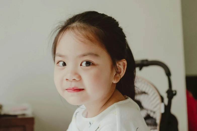 a close up of a child's face with a stroller in the background, pexels contest winner, mingei, asian beautiful face, girl cute-fine-face, slightly - pointed ears, big cheeks