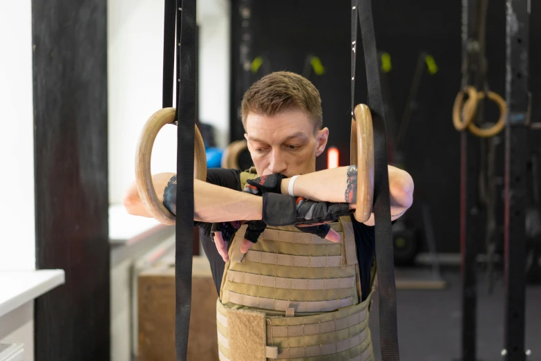 a man doing pull ups in a gym, a portrait, by Lee Loughridge, pexels contest winner, private press, body armour, neck shackle, holding a wooden staff, model is wearing techtical vest