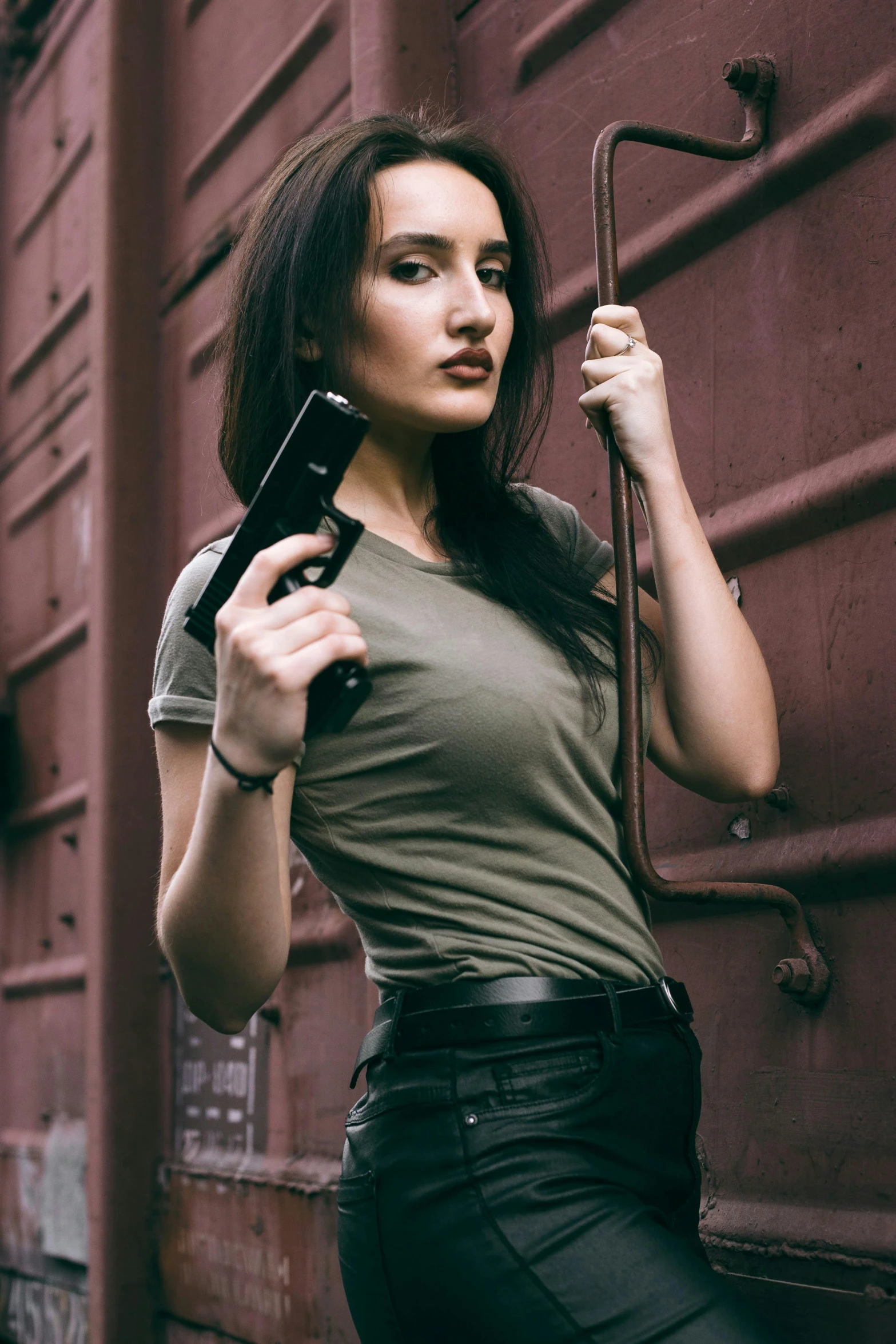 a woman standing next to a train holding a gun, a portrait, by Adam Marczyński, pexels contest winner, brunette woman, wearing a tee shirt and combats, elegant pose, better known as amouranth
