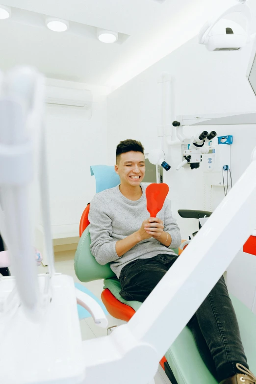 a man sitting in a chair in a dentist's chair, inspired by Tooth Wu, colour corrected, in white room, for junior, looking confident