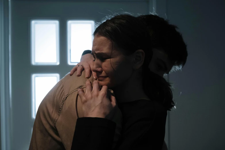 a man standing next to a woman in a dark room, by Emma Andijewska, serial art, hugging each other, production still, lgbtq, woman with braided brown hair