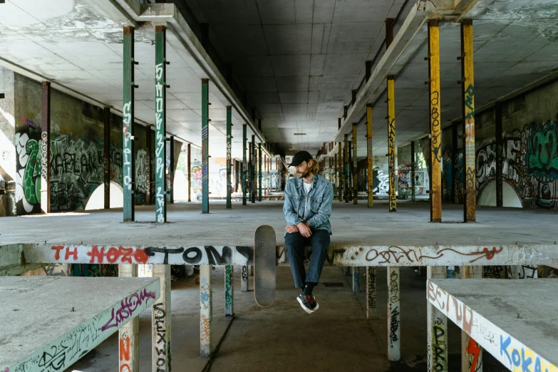 a person sitting on a bench with a skateboard, a portrait, unsplash contest winner, graffiti, in an abandoned mall, structure : kyle lambert, portrait full body, overpass