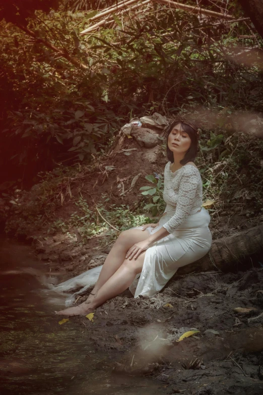 a woman in a white dress sitting on the ground, inspired by Elsa Bleda, pexels contest winner, sumatraism, in a jungle environment, old style photo, album cover, low quality photo