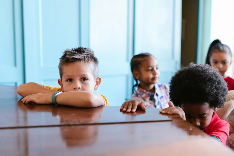 a group of children sitting at a table, by Nina Hamnett, pexels, looking off to the side, half turned around, boy with neutral face, slide show