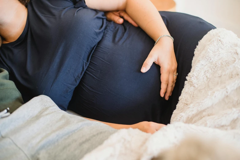 a pregnant woman laying on top of a bed, unsplash, manuka, woman holding another woman, swollen veins, sitting on a couch