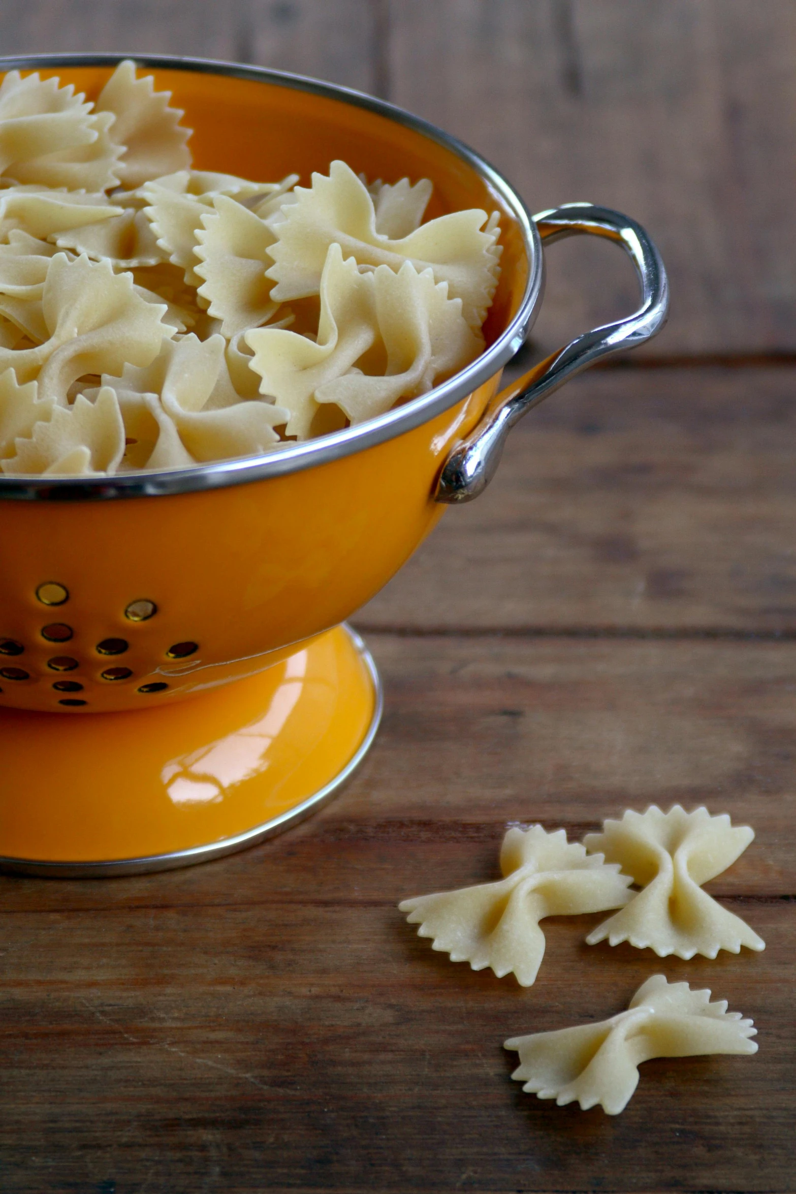 a yellow colander filled with pasta on top of a wooden table, bowknot, crisp image, kailee mandel, made of glazed